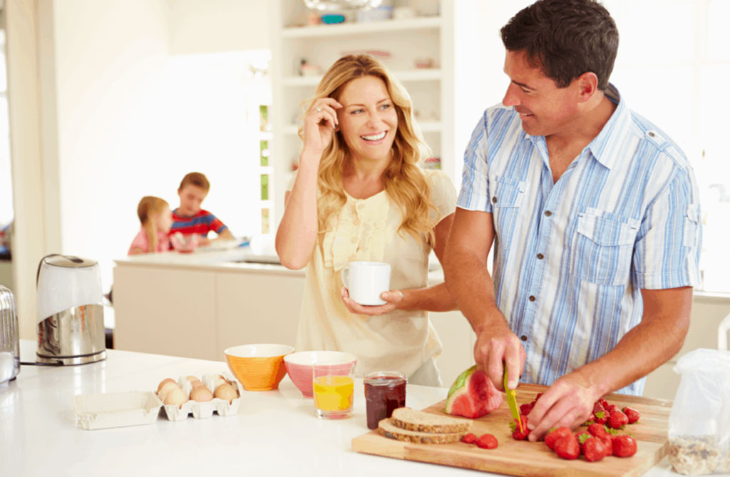 Families Couple smiling while chopping vegetables with kids in the background